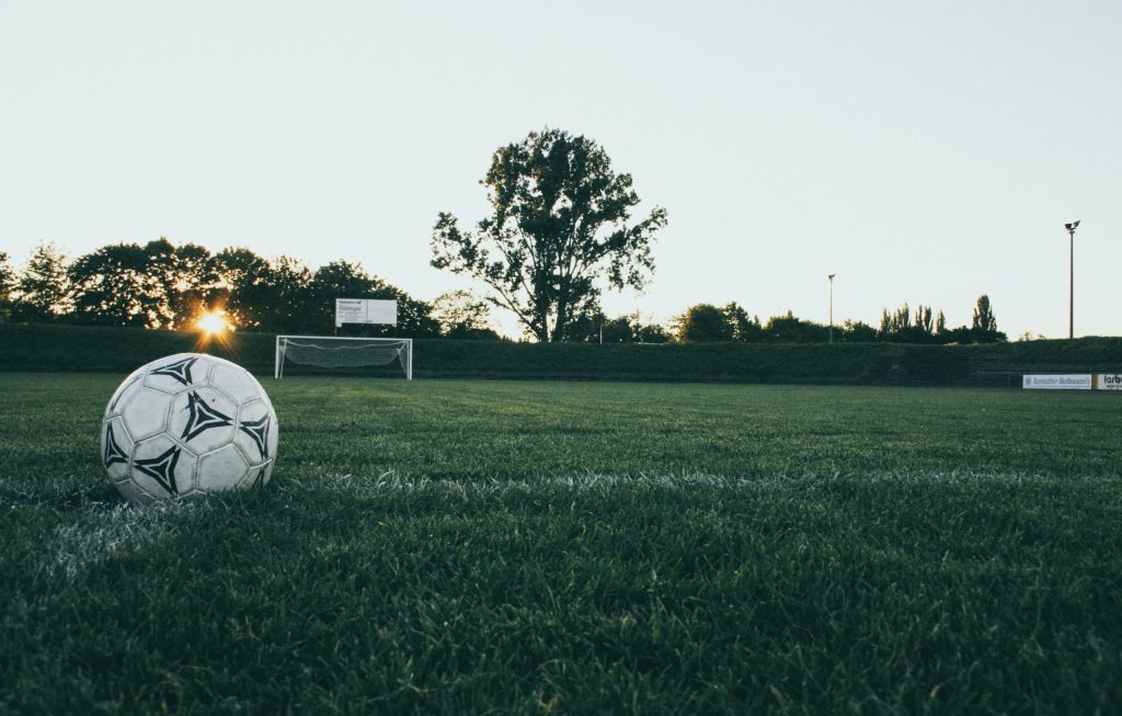 Soccer ball on field at sunrise, serene landscape with goalpost in background.